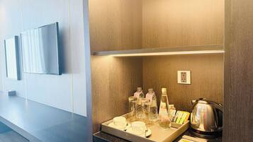 Une chambre d’hôtel dotée d’un téléviseur à écran plat fixé au mur, d’un coin café avec une bouilloire et des tasses, et d’un mur recouvert de panneaux en bois.
