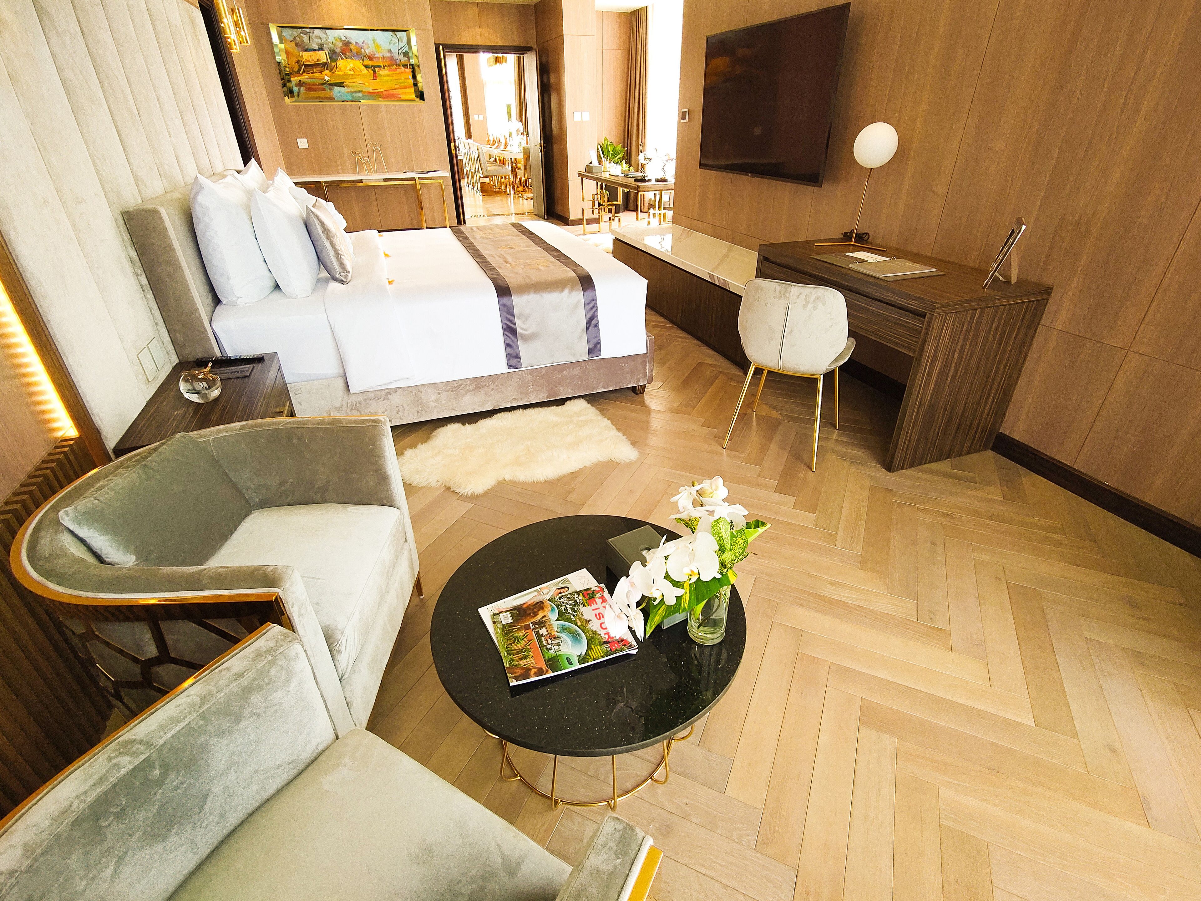 Une chambre d’hôtel moderne équipée d’un lit, d’un canapé, d’une table basse agrémentée de fleurs, d’un bureau et d’une télévision.