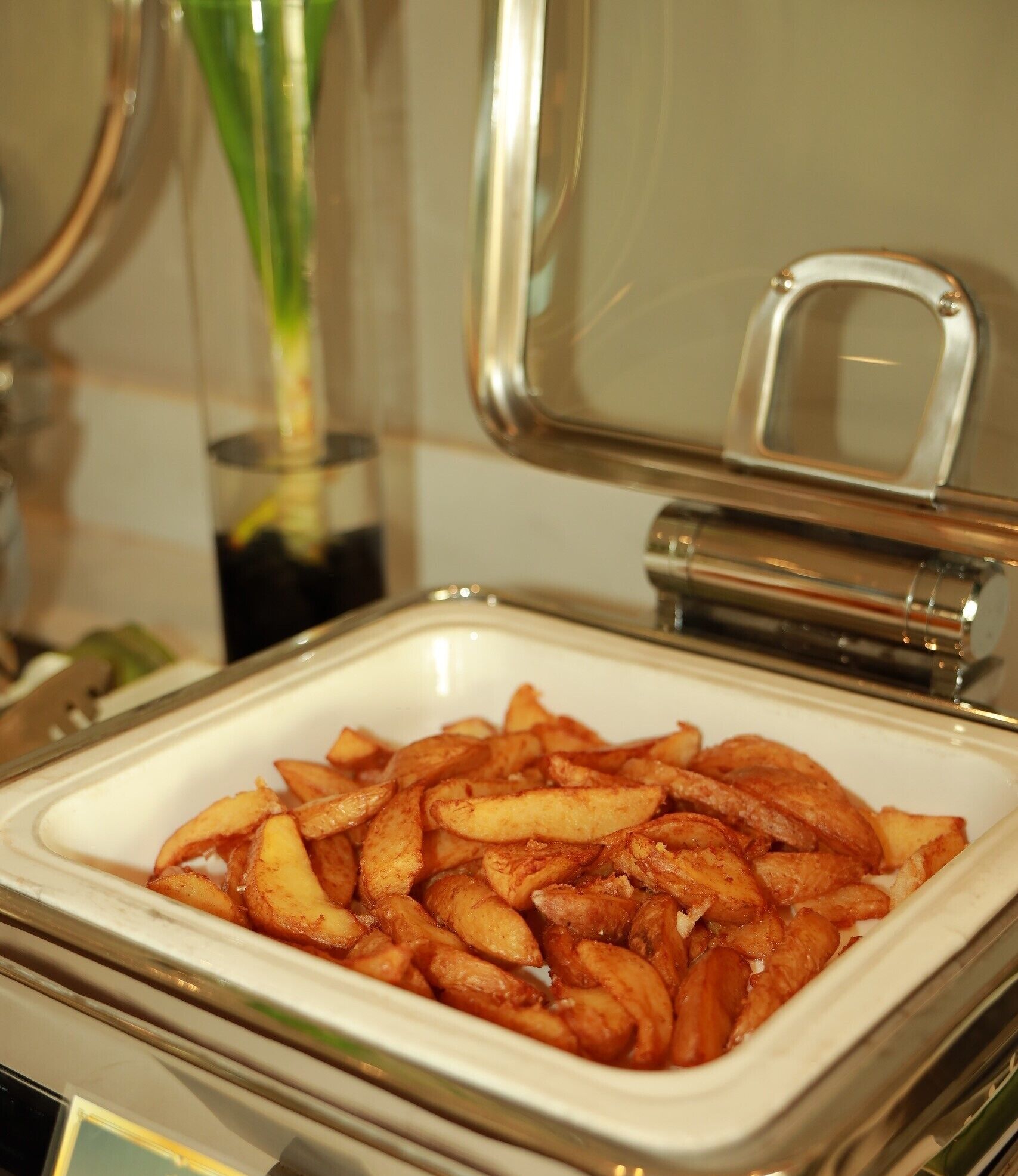 A buffet table with a white bowl filled with golden-brown potato wedges.