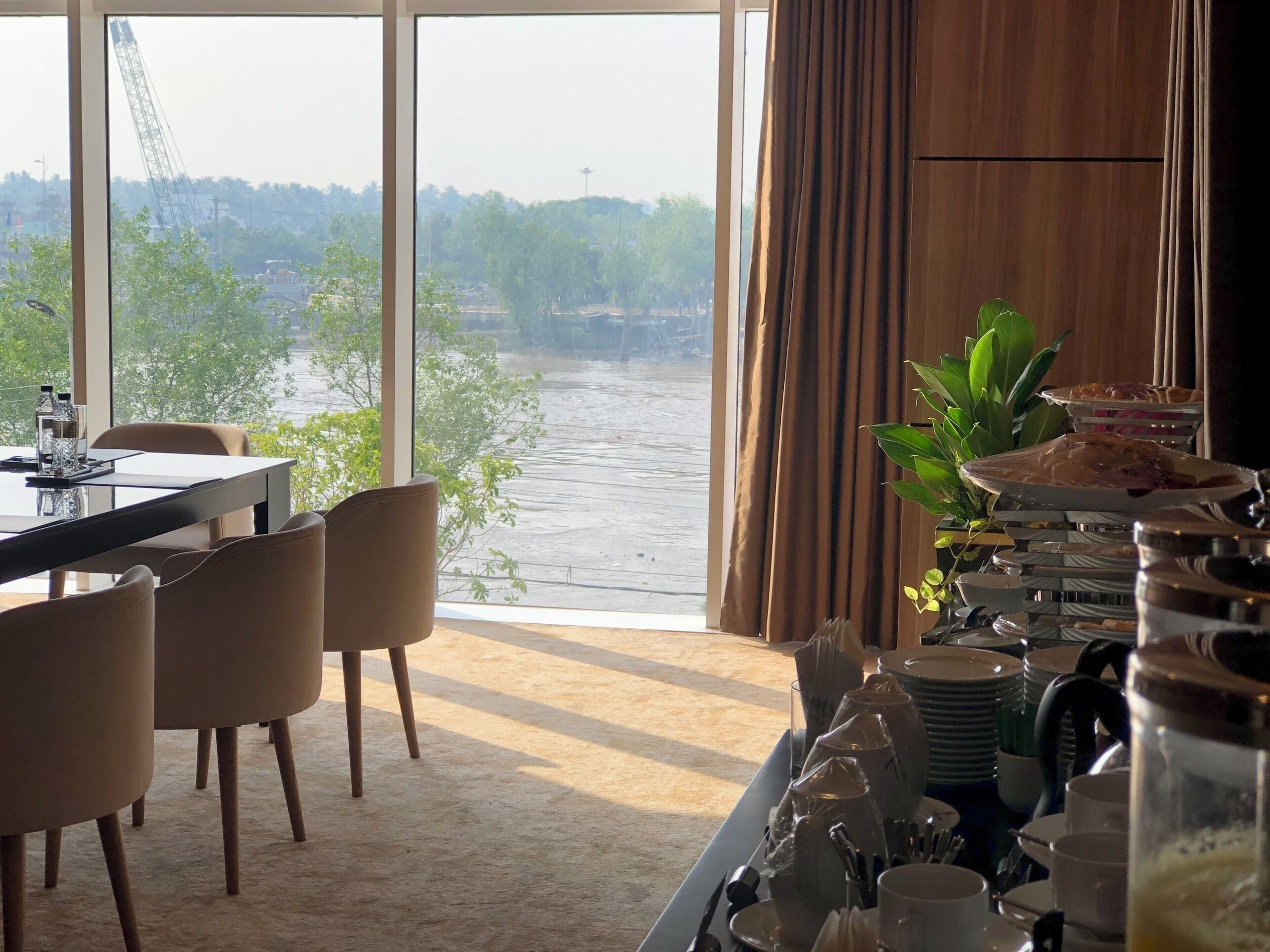 Un área de comedor con vista al río, una mesa dispuesta con platos y vasos, y una planta a un lado.