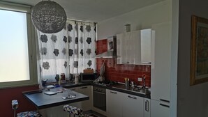 Een moderne keuken met witte kastjes, een rode spatwand, een magnetron en een gasfornuis. Er zijn twee krukken met gestreepte zittingen en een hangende lamp.