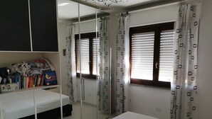 Een slaapkamer met een bed, nachtkastje, kledingkast met spiegel en raam met gordijnen.