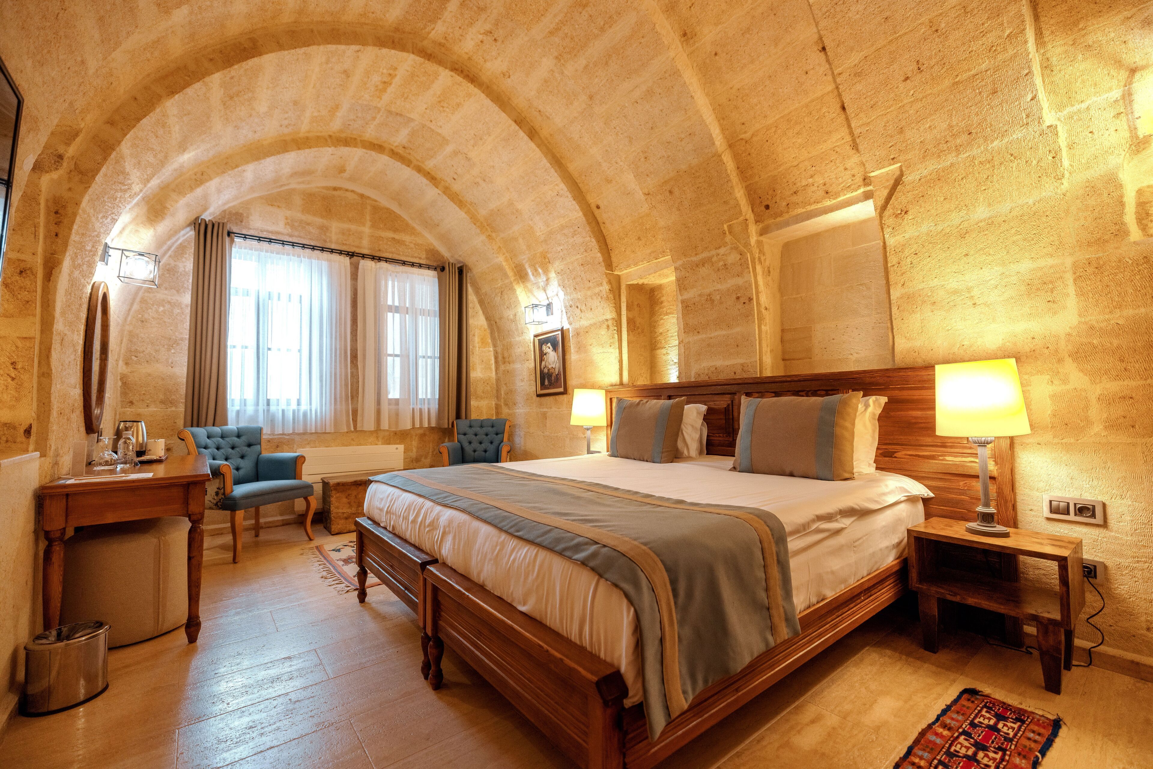 Una habitación de hotel con una cama grande, un escritorio de madera, una silla y una mesita de noche con lámpara.