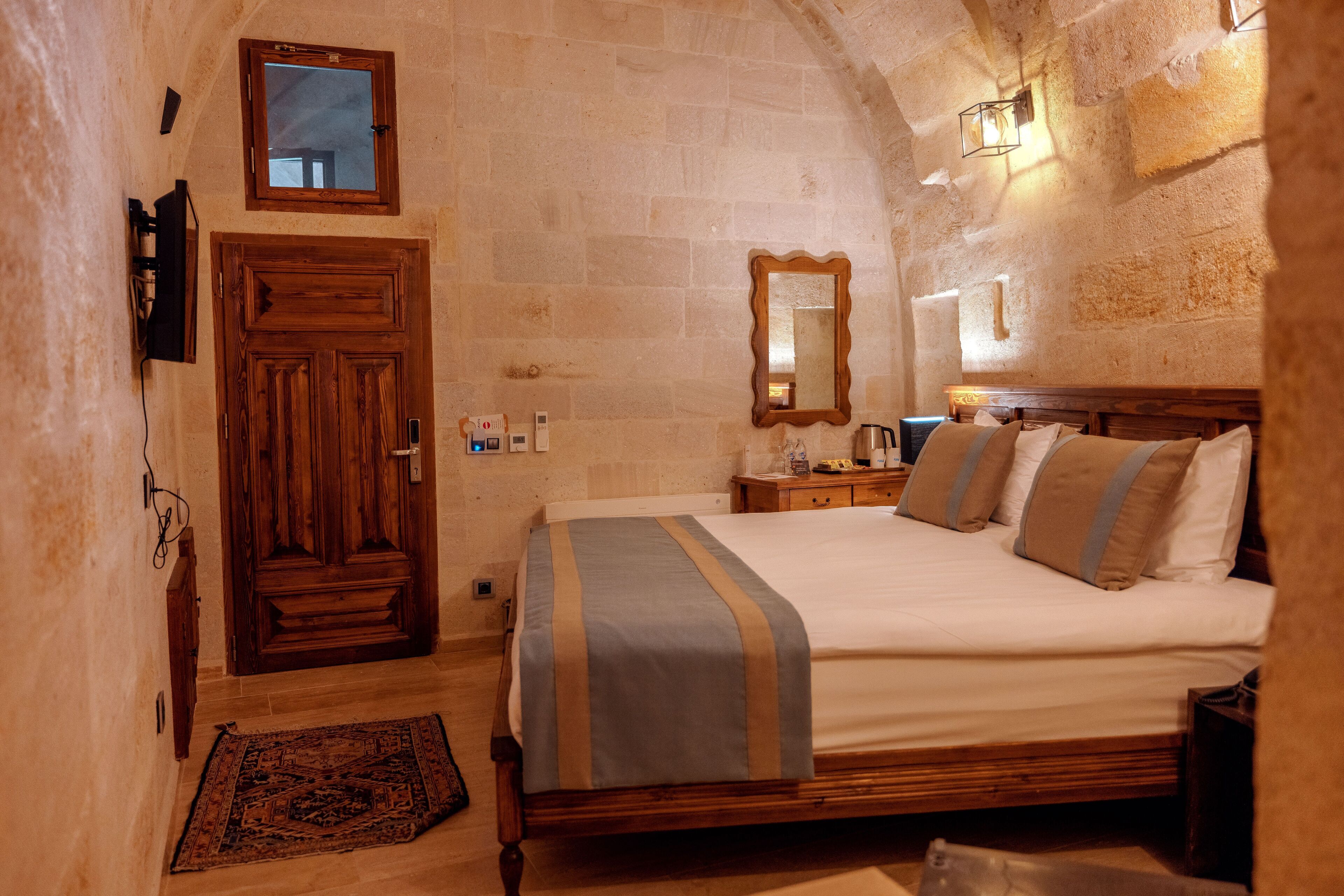 A bedroom with a wooden bed, a nightstand, a mirror, and a stone wall.
