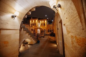 A stone archway leading to a building with a staircase and a door.