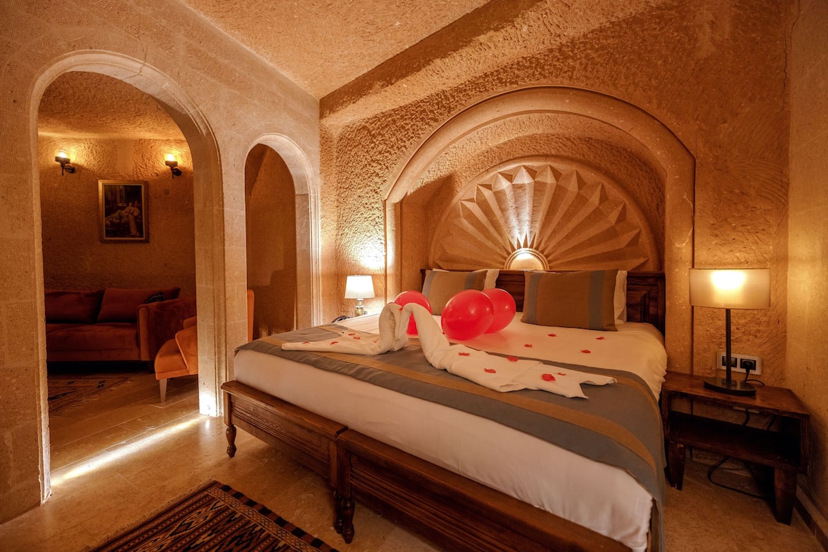 A hotel room with a large bed, a wooden headboard, two wall sconces, and a small bedside table.