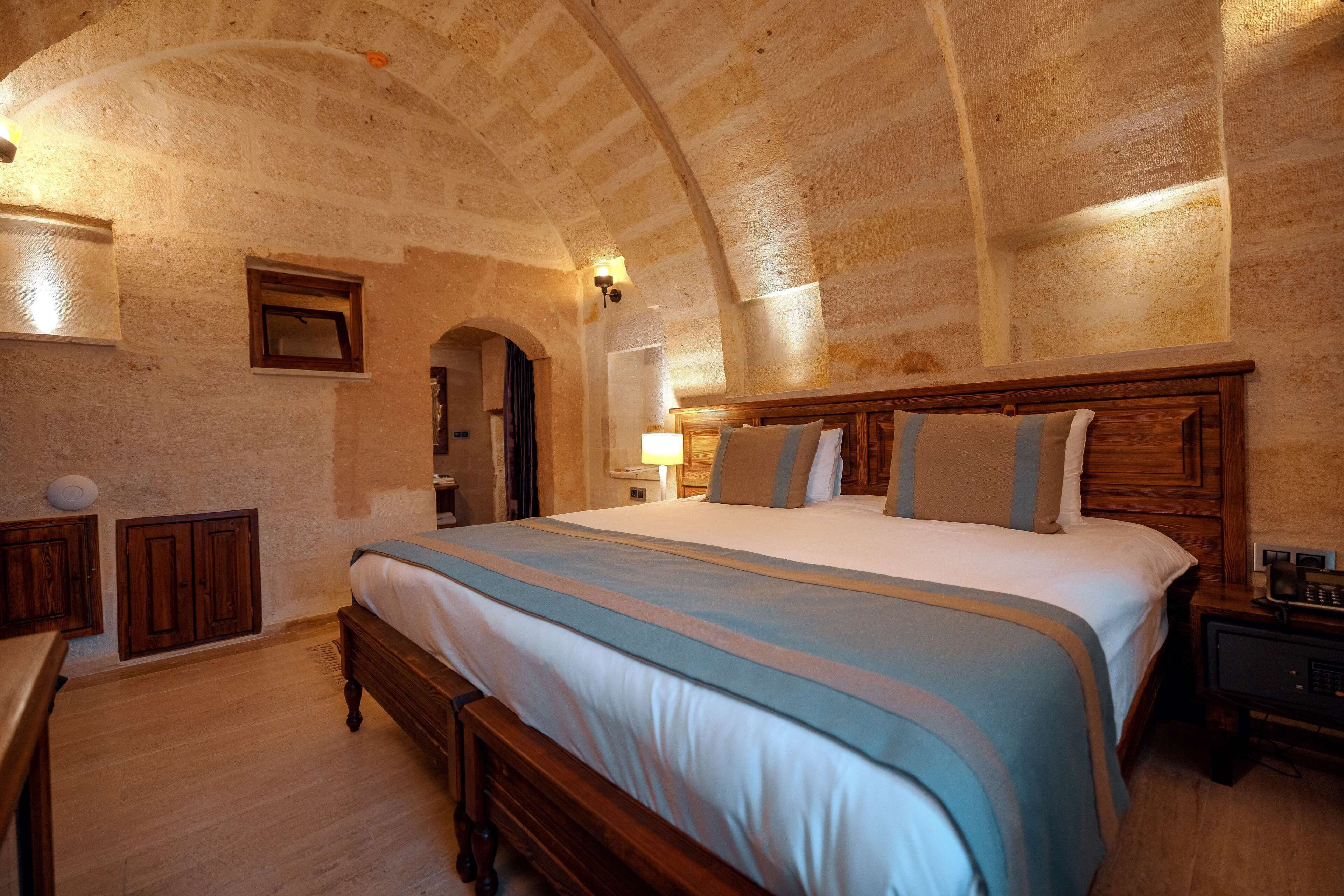 A bedroom with a large bed, wooden headboard, and a stone ceiling.
