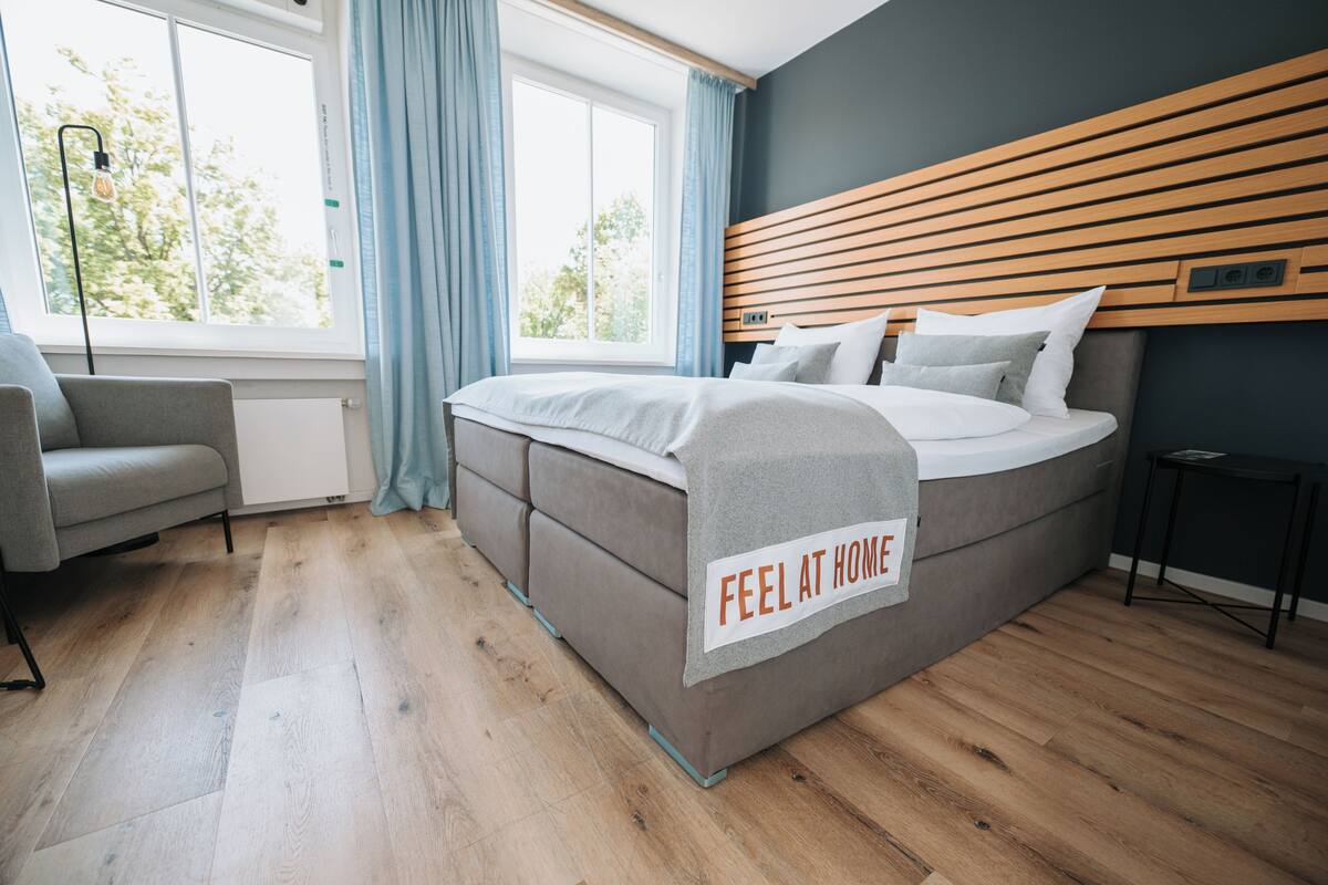 Un dormitorio moderno con una cama grande, una mesita de noche, una silla y una ventana con cortinas.