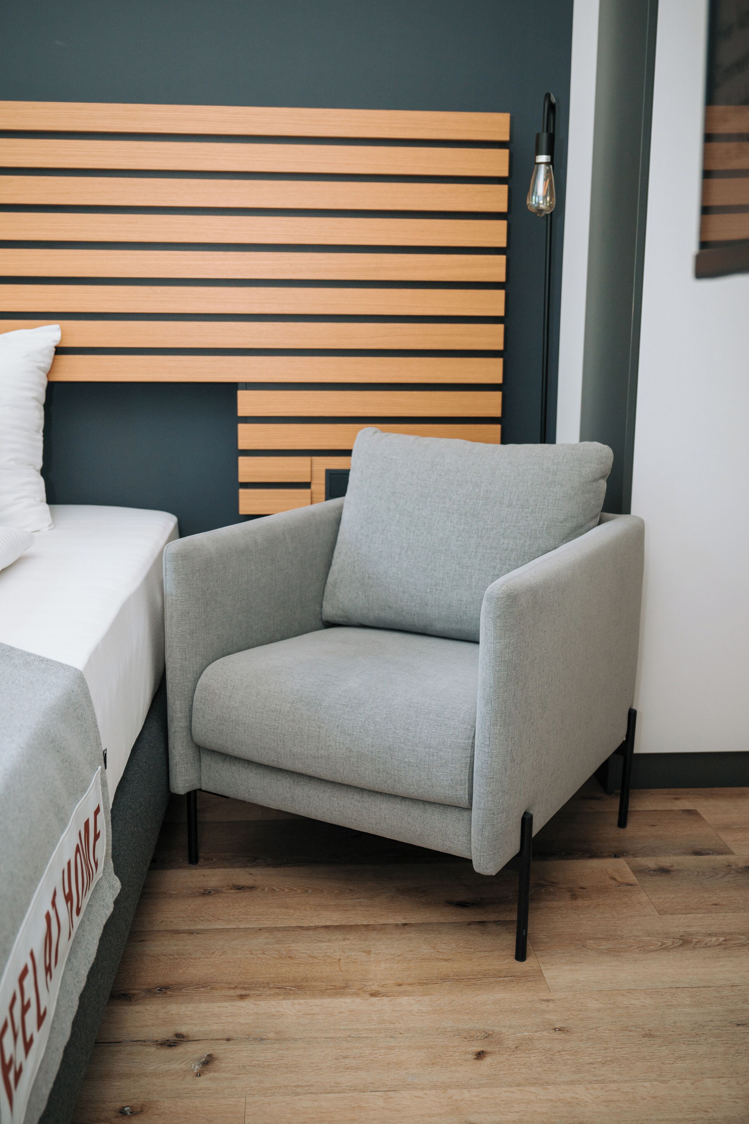 Una camera da letto moderna con una testiera in legno, una poltrona grigia, un letto bianco e un comodino.