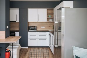 A compact kitchen with white cabinets, a microwave, a refrigerator, and a wooden countertop. - Coffee Fellows Hotel & Longstay (Pfaffenhofen an der Ilm)