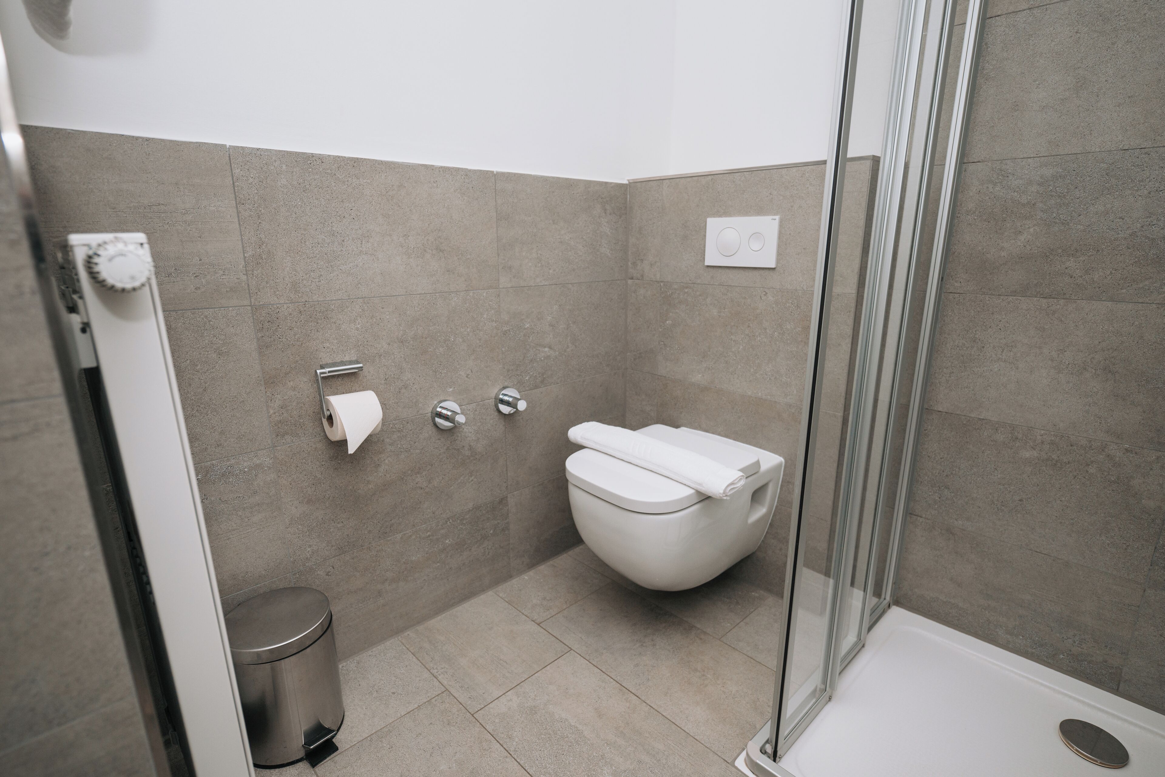 A modern bathroom with a toilet, a trash bin, and a shower area.