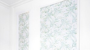 A dining area with a glass table and green upholstered chairs, white walls, and a bamboo leaf pattern wallpaper.