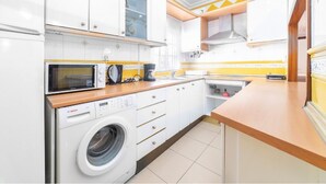 A compact kitchen with white cabinets, a Bosch washing machine, a microwave, and a sink.