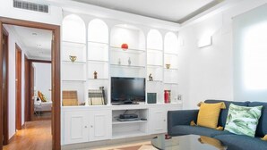 A modern living room with a blue sofa, a glass coffee table, and a white entertainment unit with shelves.