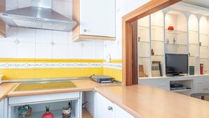 A kitchen with a stainless steel range hood, a yellow and white tiled backsplash, a wooden countertop, and a built-in TV shelf.