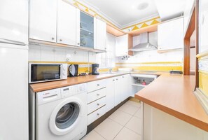 A compact kitchen with white cabinets, a Bosch washing machine, a microwave, and a sink.