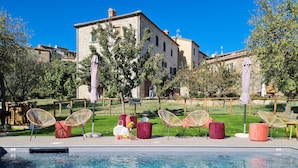 A pool area with lounge chairs and a stone building in the background. - Agriturismo La Via dell'Oliviera (Chiusdino)