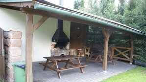 Un patio al aire libre con chimenea de ladrillo, bancos de madera y una zona cubierta.