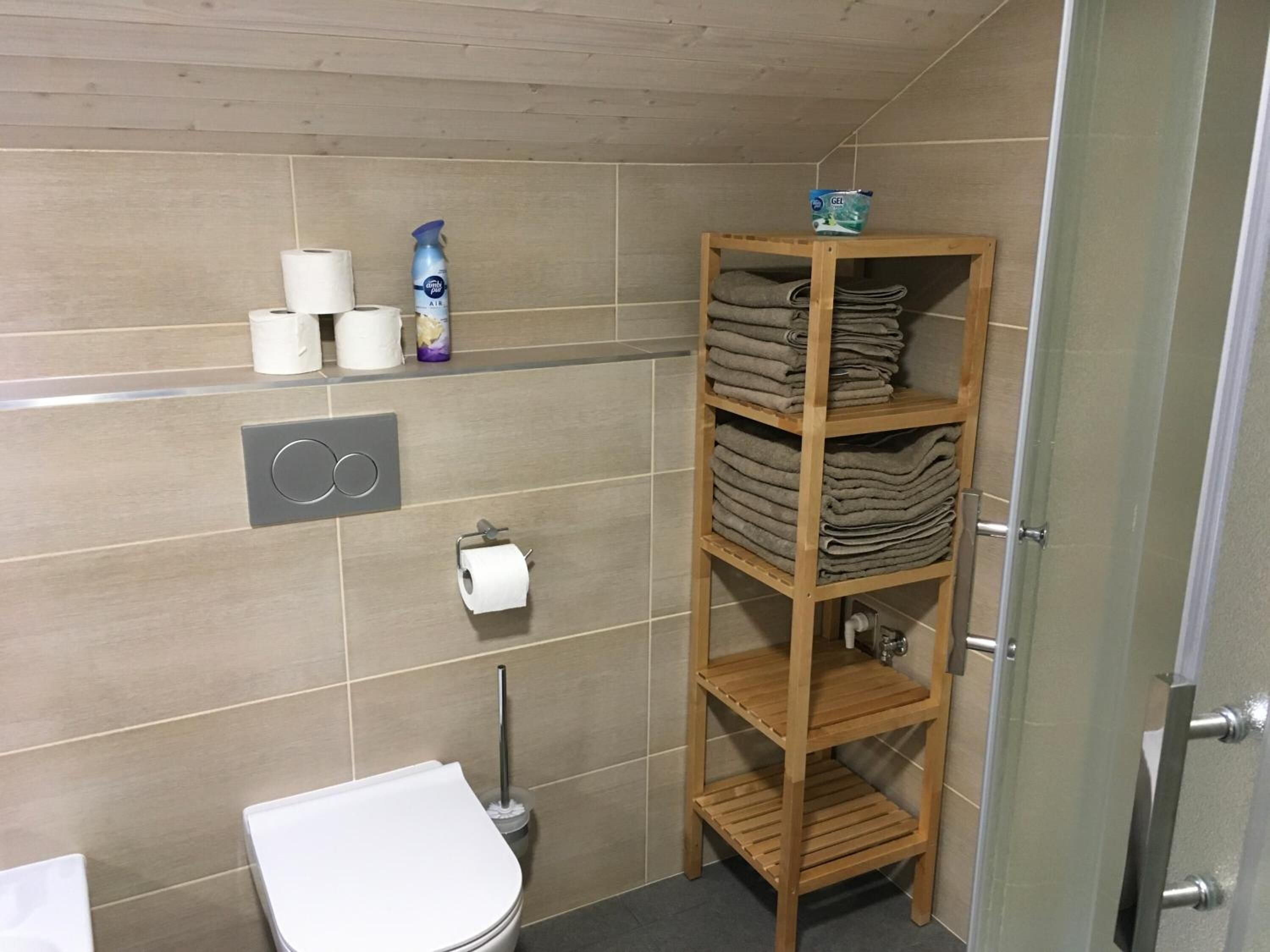 A bathroom with a toilet, a shelf with folded towels, and a roll of toilet paper.