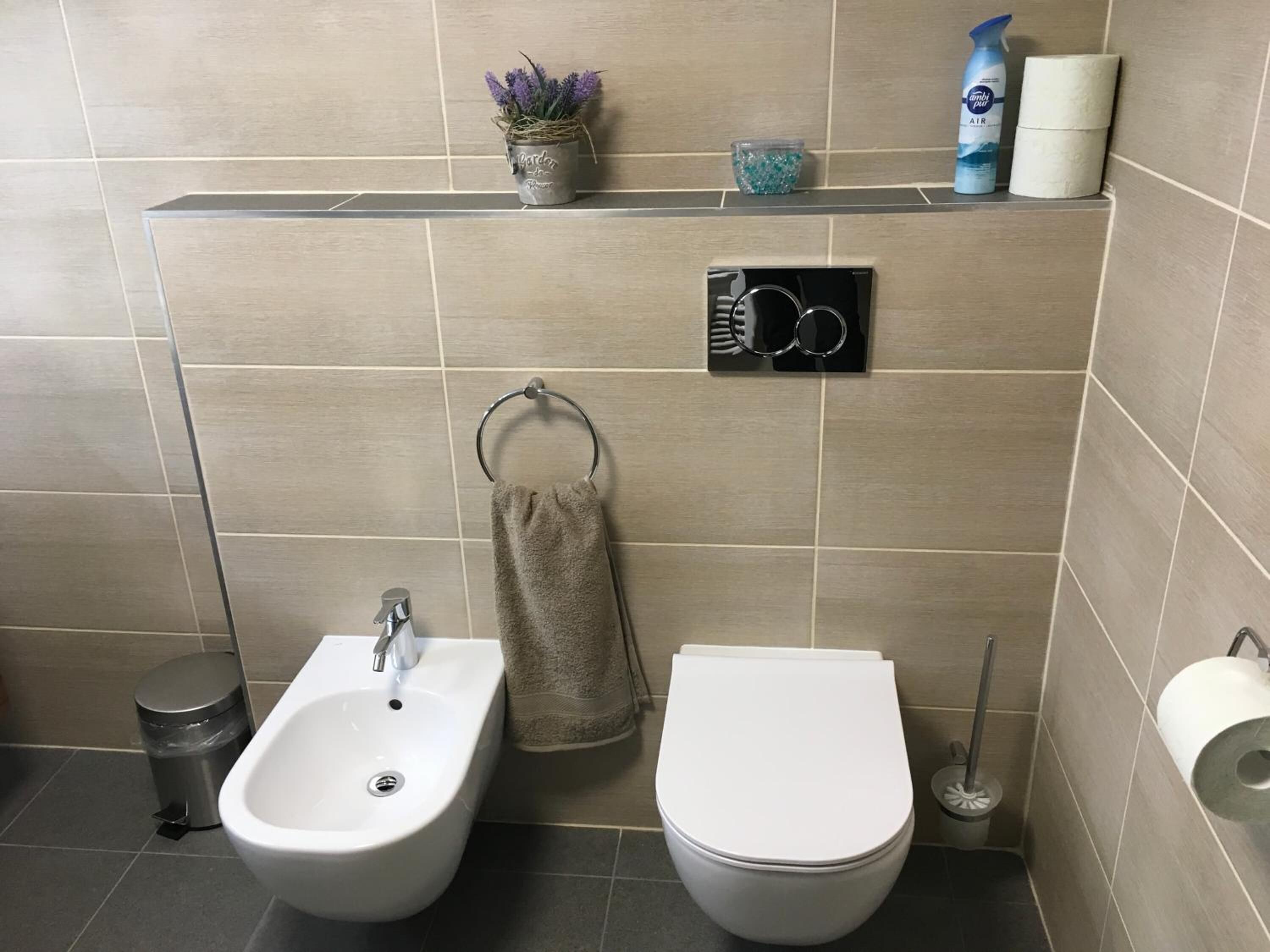 Een moderne badkamer met een toilet, een hygiëneschuimer en een plank met toiletartikelen.