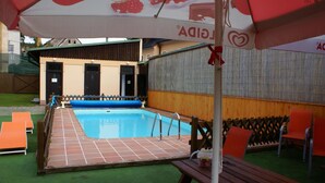Zona de piscina con terraza de madera, sillas reclinables anaranjadas y una mesa de picnic.