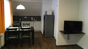 Un espacio habitable compacto con zona de comedor, kitchenette y televisor montado en la pared.
