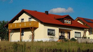 Una casa de dos pisos con techo rojo, un balcón y un pequeño porche.