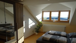 Un dormitorio con cama, un espejo grande, una planta en maceta y una ventana con vista a edificios.