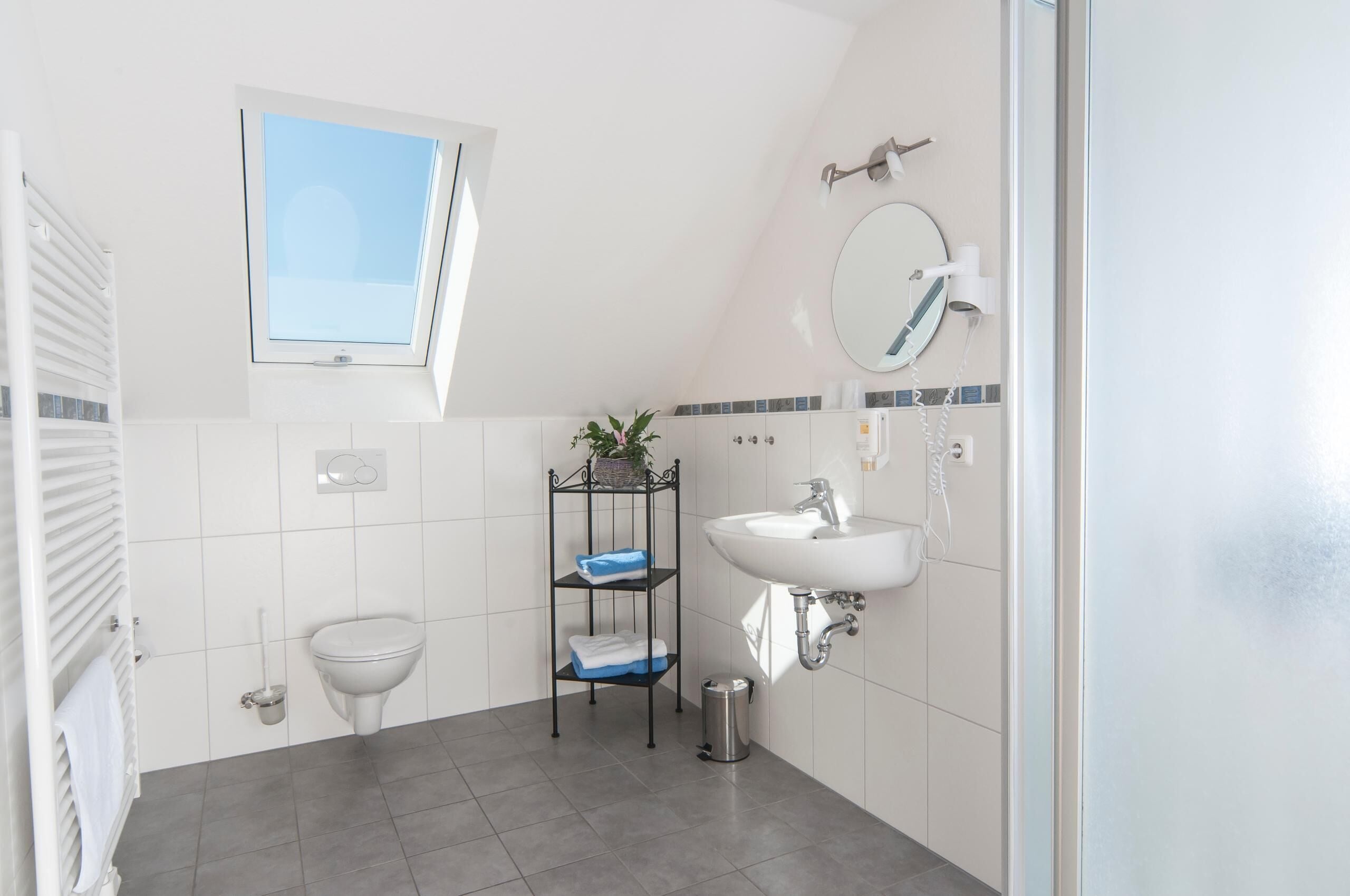 Un baño con inodoro, lavabo, espejo, ventana y repisas con toallas.