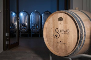 A wooden barrel with the label "Schwab Das Weingut" and a row of metal wine tanks in the background. - Pension Weingut Schwab (Thuengersheim)