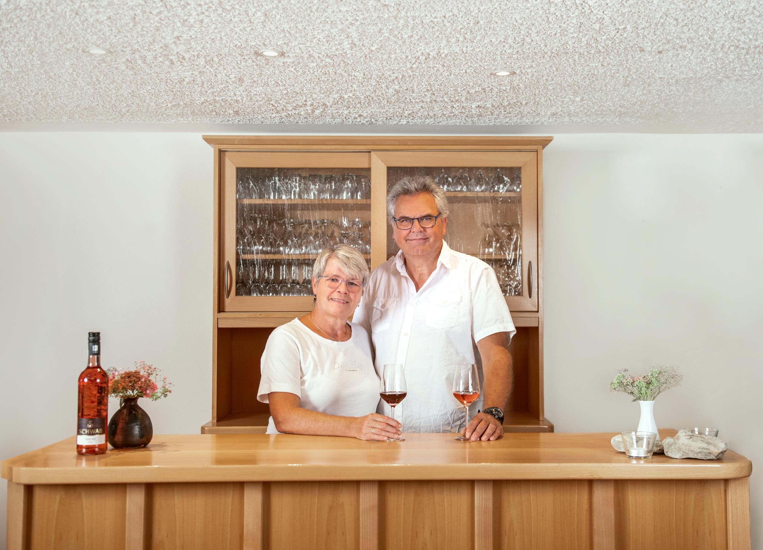 Eine Barbereich mit Holztresen, einem Schrank für Gläser und einer Weinflasche.