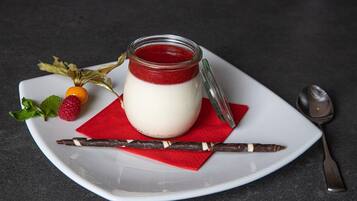 A dessert with a red jelly layer, a white creamy layer, and a chocolate stick on a white plate with a red napkin.