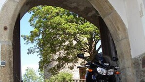 Una motocicleta estacionada bajo un arco, con un edificio y árboles al fondo.