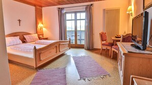 Habitación de hotel con cama de madera, escritorio con computadora, silla, televisor y ventana con cortinas.