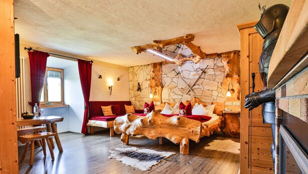 Una habitación rústica con una cama de madera, pared de piedra y chimenea.