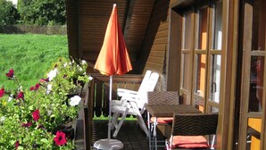 A wooden deck with outdoor furniture, including chairs and a table, and a large umbrella. - Ferienwohnung Bücherl (Waldmuenchen)