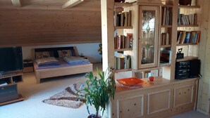 A cozy living room with a bed, a TV, a bookshelf, and a potted plant. - Ferienwohnung Bücherl (Waldmuenchen)
