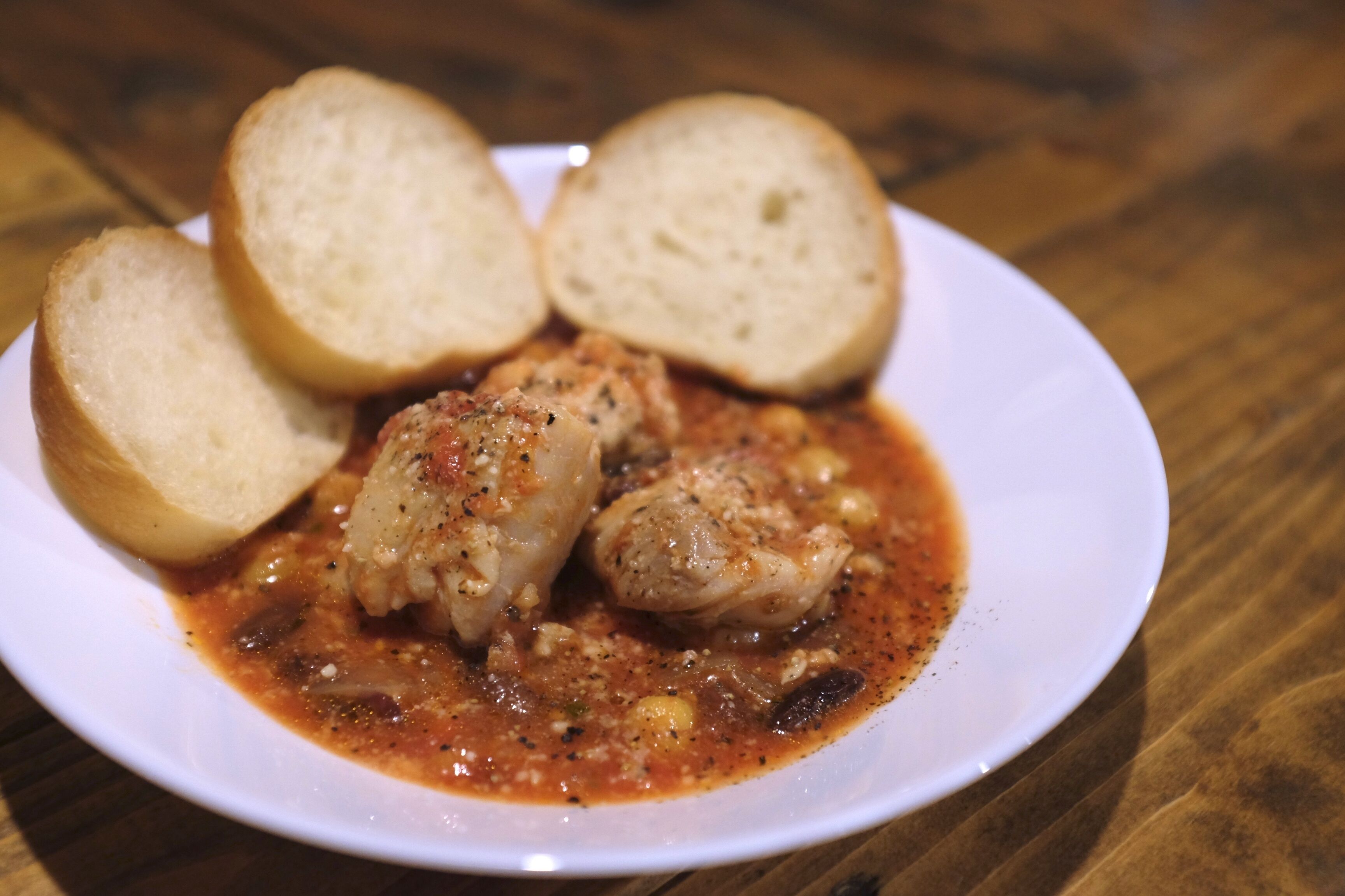 A plate of chicken with sauce and bread on a wooden table.