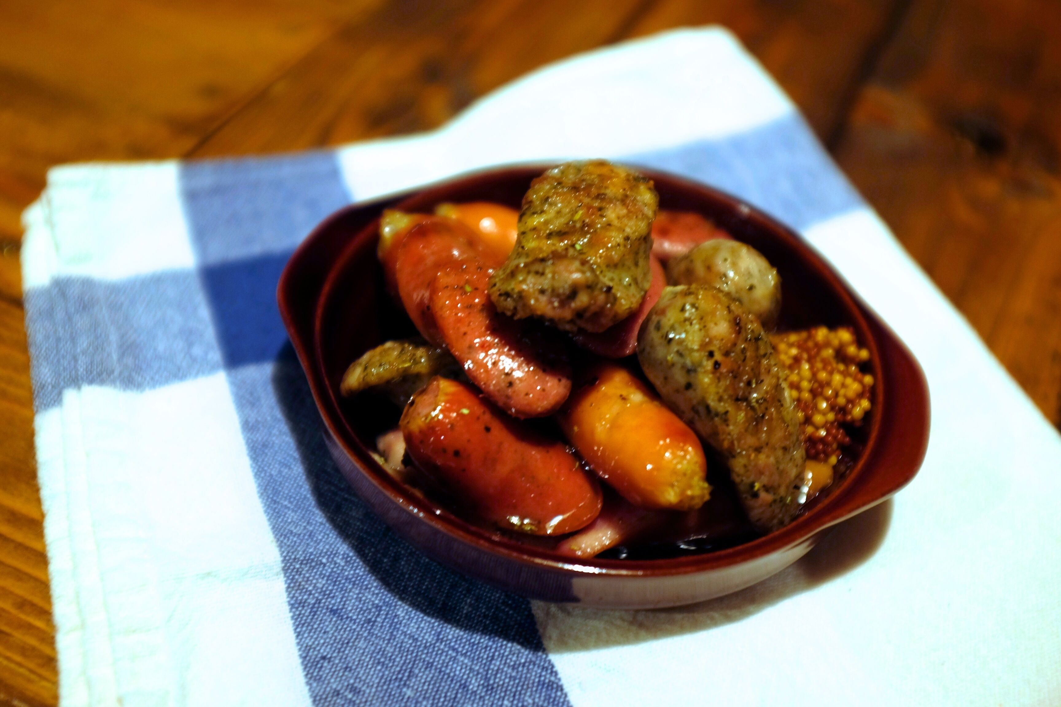 A bowl of food with sausages and vegetables on a checkered napkin.