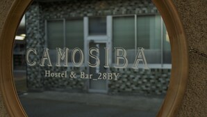 A mirror reflecting the name "CAMOSIBA Hostel & Bar 28BY" on a building facade.