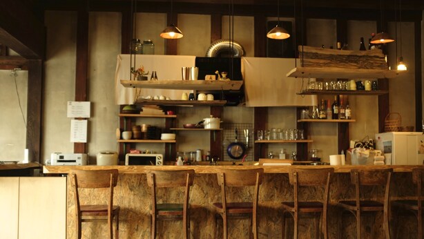 A bar area with wooden chairs and shelves stocked with bottles and glasses.