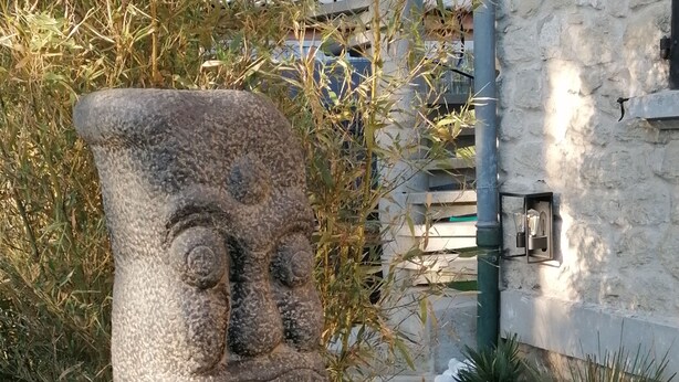 A stone sculpture with a face, surrounded by plants and a stone wall.