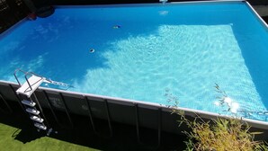 A rectangular above-ground pool with a ladder on one side, surrounded by a fence and greenery.