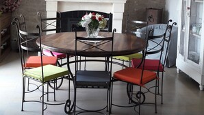 A dining area with a round table, four chairs, a white fireplace, and hanging light fixtures.