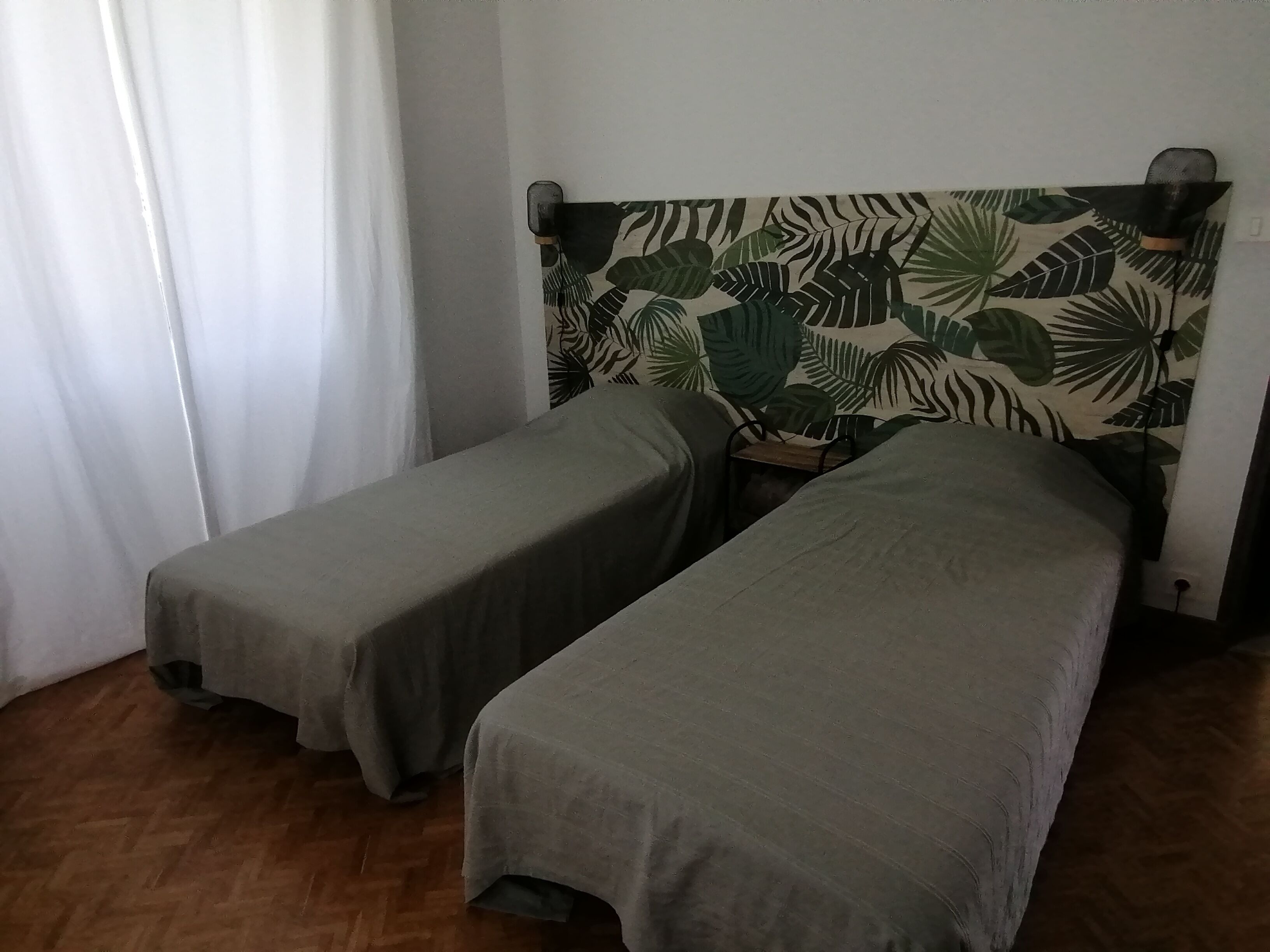 A room with two single beds, a wooden floor, and a headboard with a leaf pattern.