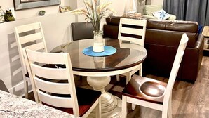 A modern living room with a round dining table, white chairs, a brown leather sofa, and a TV mounted on the wall. - Coligny Beach- spacious 3 bed condo super clean and close to everything Coligny! (Hilton Head)