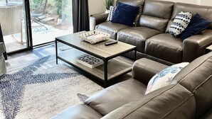 A modern living room with a brown leather sofa, a coffee table, and a ceiling fan. - Coligny Beach- spacious 3 bed condo super clean and close to everything Coligny! (Hilton Head)
