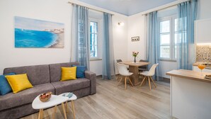 A modern living room with a grey sofa, a dining table with chairs, and a kitchen area. - Old city top spot apartments just one step from the main street Stradun (Dubrovnik)
