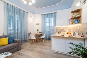 A modern living room with a sofa, dining table, and chairs. There is a kitchen area with a counter and appliances.