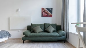 A modern living room with a green sofa, a painting on the wall, and a window with curtains.